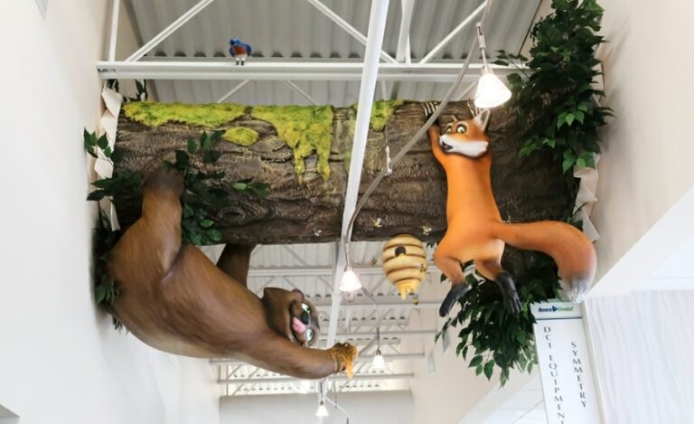 Comical, hallway ceiling sculpture of fox slipping from a tree trunk while a bear steals honey from a beehive.