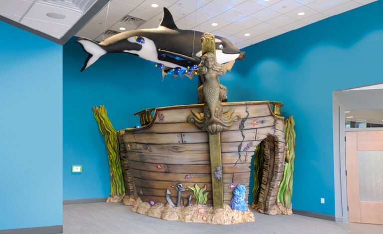 Shipwreck themed play area with sculpted sunken ship entrance and orca whale suspended from the ceiling.