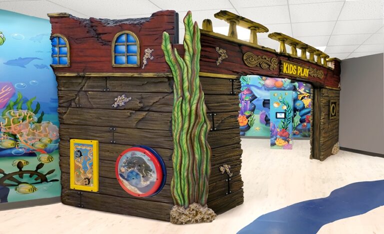 Ocean-themed kid's play area with colorful wall murals of swimming sea creatures and an enclosed space with sculpted shipwreck entrance and wall mounted play panels. creatures and an enclosed space with sculpted shipwreck and wall mounted play panels.