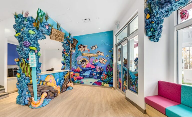 Dental office reception area with ocean-themed wall murals, window murals and sculpted coral reef and shipwreck cladding on the reception desk and ceiling area.
