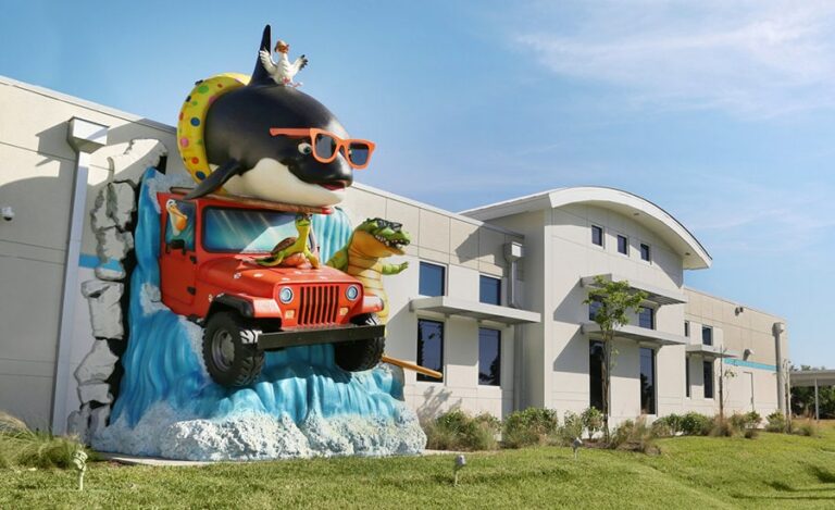 Huge, landmark, beach-themed sculpture of multiple animal mascots surfing and driving a jeep through a waterfall and appearing as though they are bursting through a dental office exterior wall.