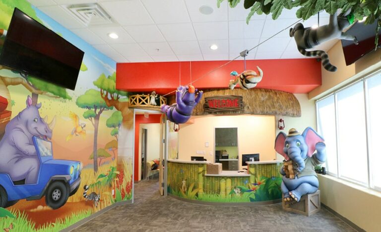 Jungle-safari themed reception area with wall murals, sculpted ziplining jungle characters, a photo-op elephant on a crate with tiki-hut style reception desk.