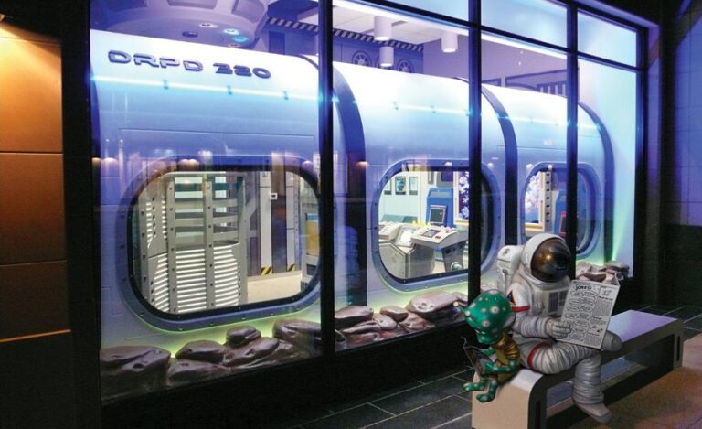 Space-themed photo-up sculpture of an astronaut and alien reading the paper while seated on a bench.