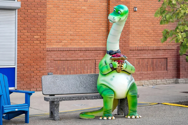Green dinosaur sculpture beside a bench and flower planter in downtown Drumheller, Alberta