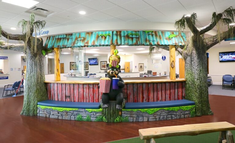 Interior cladded bench seating between two large mossy trees with 3D photo op characters posed in the middle.