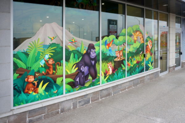 Storefront windows display a colorful jungle mural featuring gorillas, monkeys, tigers, leopards, birds, and lush green plants, with a mountain.