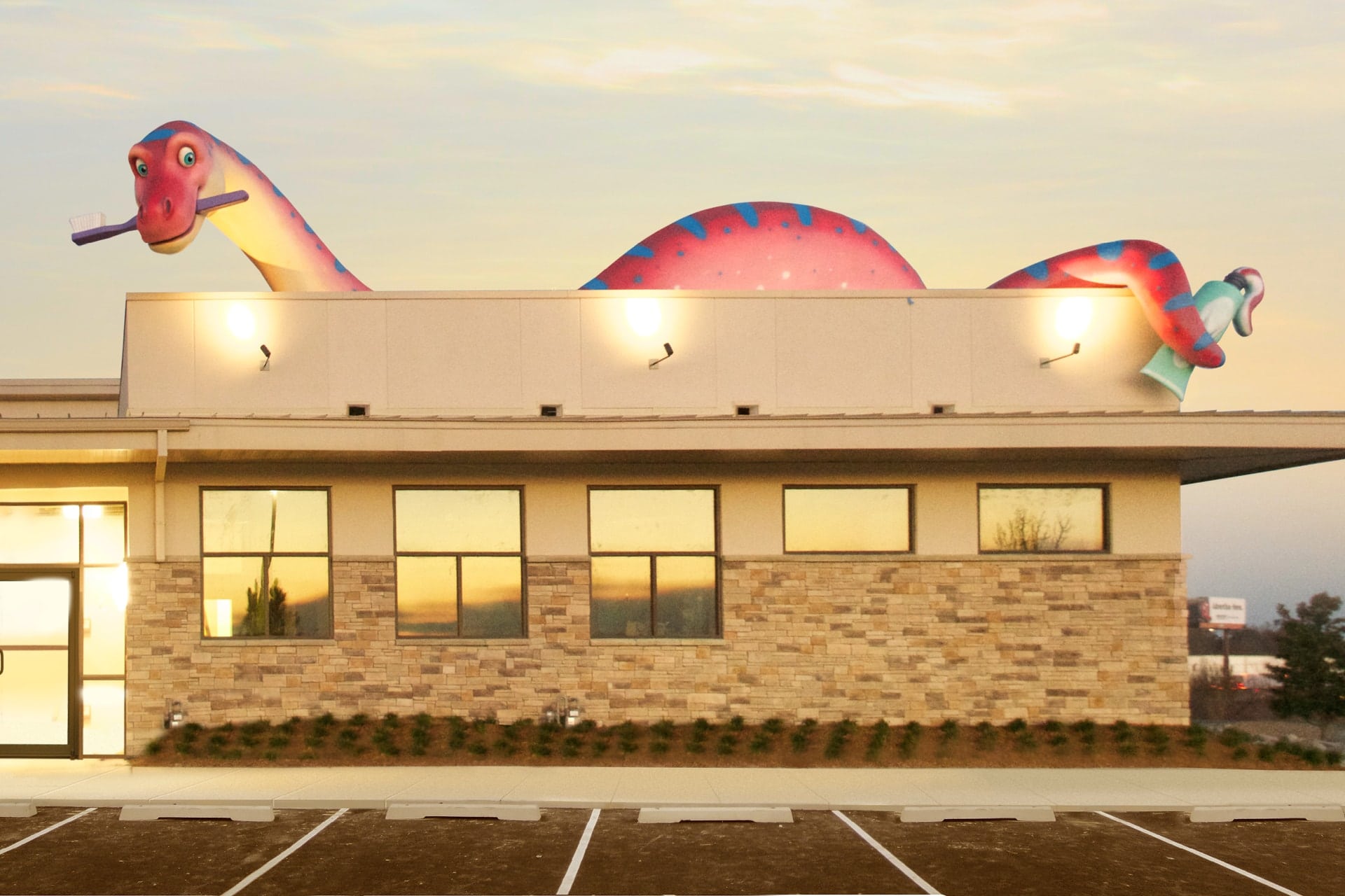 Before and after a themed environment transformation, a large, colorful sculpture of a smiling dinosaur holding a toothbrush now sits atop the tan brick dental office, glowing warmly in the sunset.