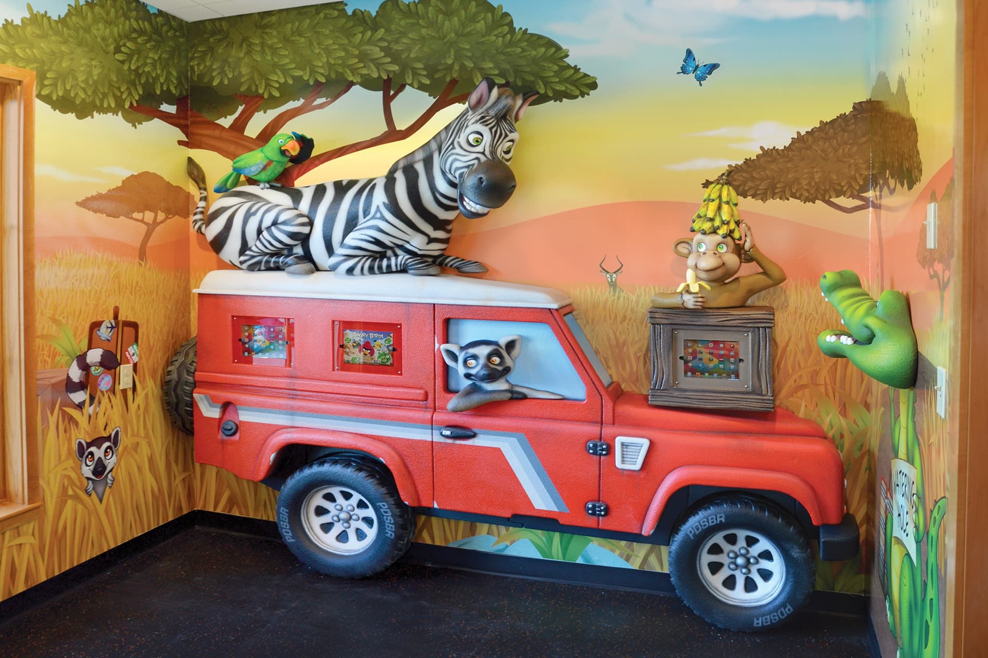 Experience a stunning themed environment transformation in this colorful safari-themed kids playroom. Before and after, the red jeep, vibrant mural animals, and playful creatures bring adventure and excitement to life.