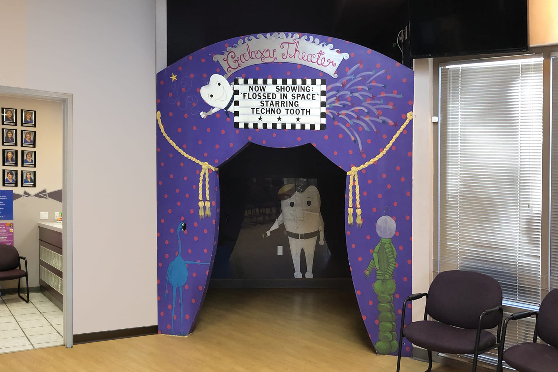 A drab, hand-painted archway labeled Toothary Theater leads into a dark room. A sign reads Now Showing: Flossed in Space Starring Techno Tooth. Chairs and windows are visible nearby—this is a boring before photo.
