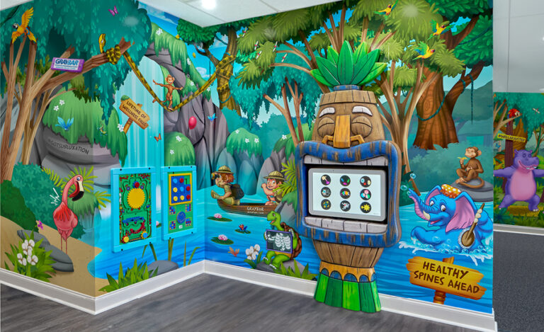Colorful children’s playroom in a chiropractor office, featuring jungle-themed wall murals, cheerful animals, interactive wall games, and a tiki statue with a touchscreen. Signs read “Healthy Spines Ahead” as monkeys swing on vines above a river.