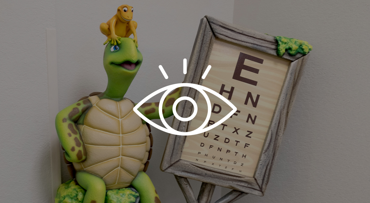 A sculpted turtle holding an eye chart in a optometrist office with a yellow sculpted frog on his head.