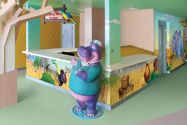 A colorful Pediatric Front Desk welcomes families, featuring a cartoon hippo statue in medical scrubs and animal-themed murals with a lion, zebra, and hippo decorating the walls and counter.