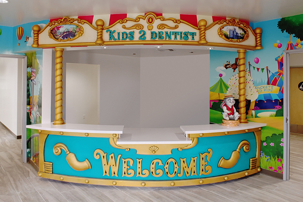 Colorful Pediatric Front Desk for a dental office, featuring a bright “WELCOME” sign, all surrounded by playful, amusement park-themed wall art and decorations.