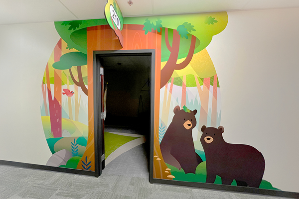 A hallway wall features a mural of a colorful forest, with two bears standing together among the trees—an inviting decor for children's hospital spaces.