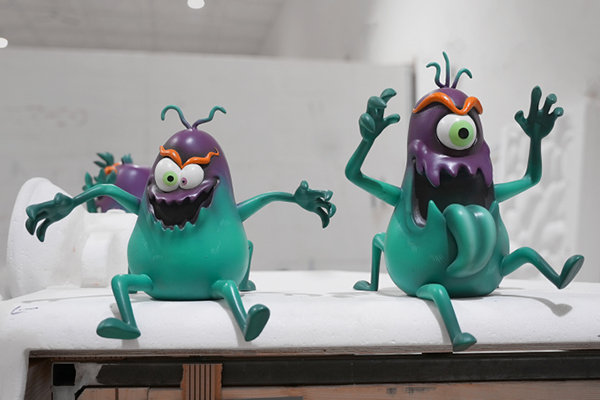 Two colorful, cartoonish tooth bug figurines with green bodies, purple heads, one large eye, and orange eyebrow. With expressive faces and outstretched arms, they are playful sugar bugs ready for an adventure in a themed dental office.