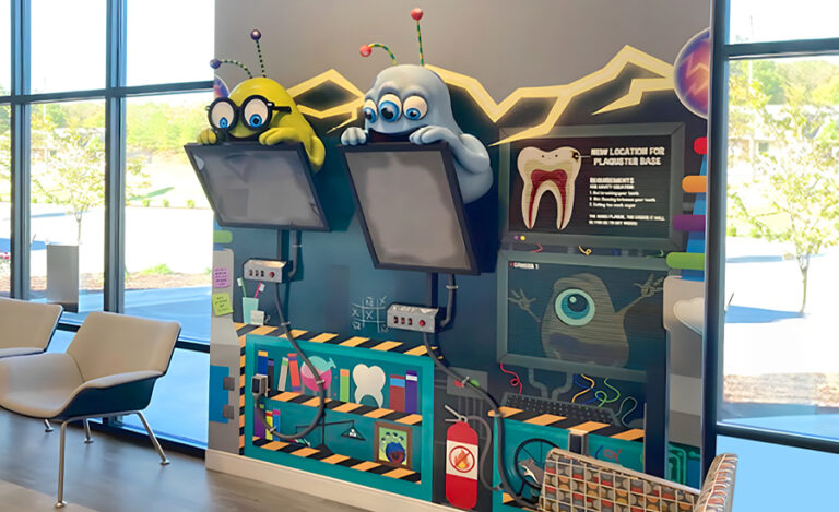 A colorful dental office kids area features two playful alien figures above mounted screens, science-themed wall graphics, and a tooth diagram, creating a fun, engaging atmosphere by large sunny windows.
