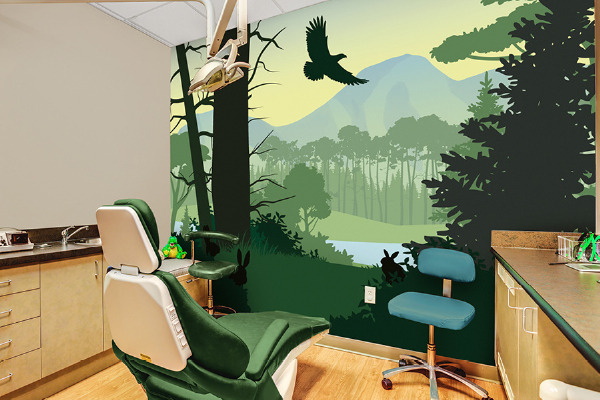A dental office room with a green dental chair, a blue stool, and a wall mural depicting a forest scene with trees, mountains, a river, and a flying bird under a yellow sky.