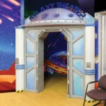 Experience a stunning themed environment transformation as the entrance becomes Galaxy Theater, featuring sci-fi decor. See the before and after: a waiting area with chairs, a counter, and vivid space murals of rockets and stars.