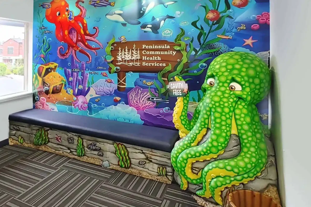Colorful underwater-themed waiting area transformed with vibrant sea creature murals and a large green octopus sculpture holding a “Cavity Free” sign. Experience a themed environment transformation at Peninsula Community Health Services.