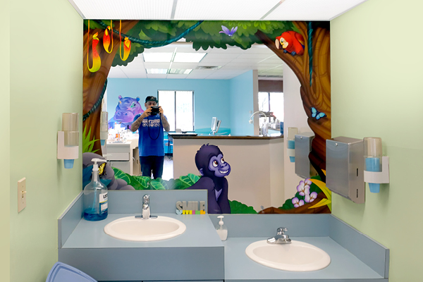 A large mirror in a brushing station decorated with cartoon jungle animals, including a smiling purple gorilla and birds. 