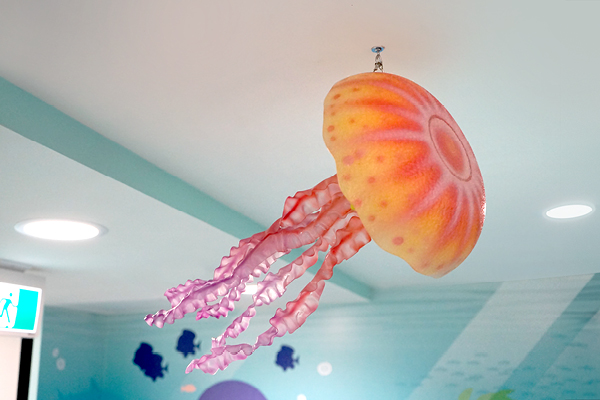 A large, colorful jellyfish decoration with pink tentacles hangs from a ceiling in a room with blue walls and ocean-themed murals.
