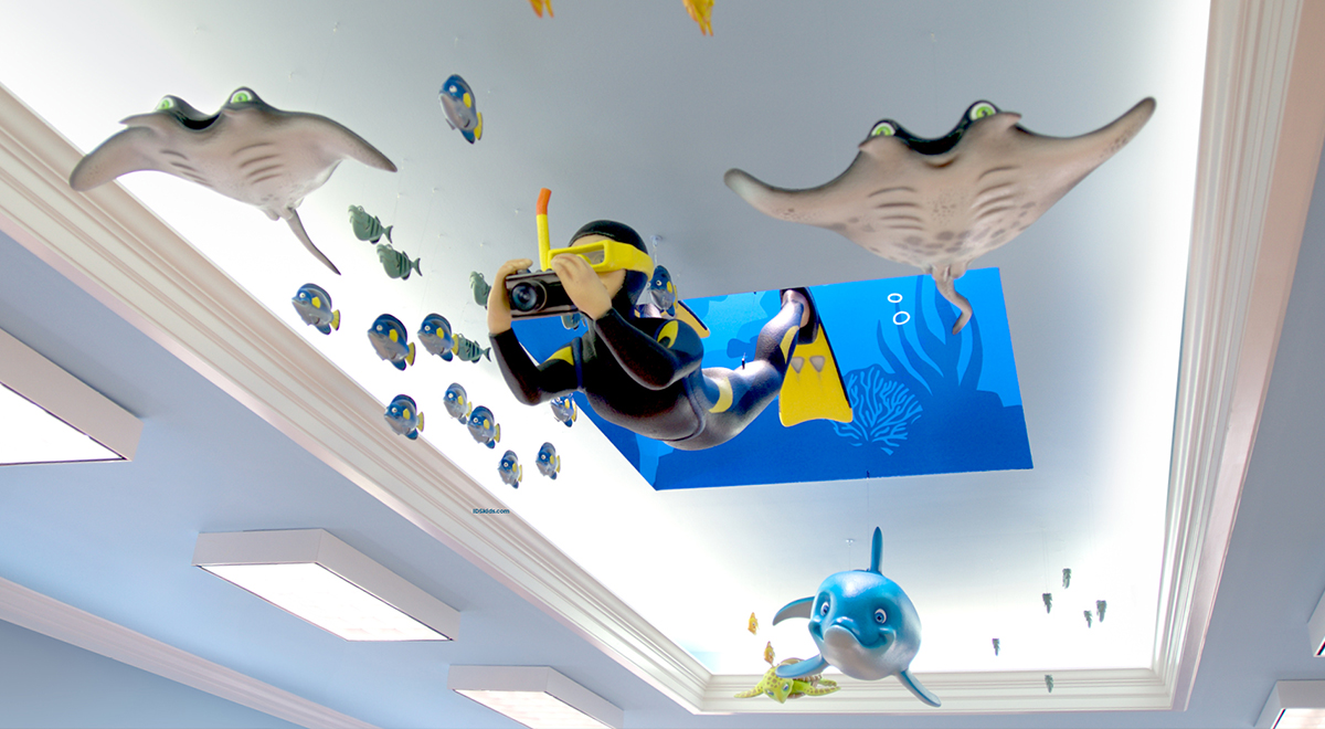 A sculpted diver and sea animals, including fish, stingrays, and a dolphin, appear to swim across a brightly lit ceiling decorated with an ocean theme.
