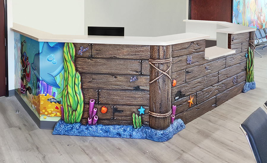 Reception desk decorated with an undersea theme, including cartoon sea creatures, coral, wooden planks, and blue water along the bottom—perfect for a welcoming swim facility. The desk is in a brightly lit room with light wood flooring.