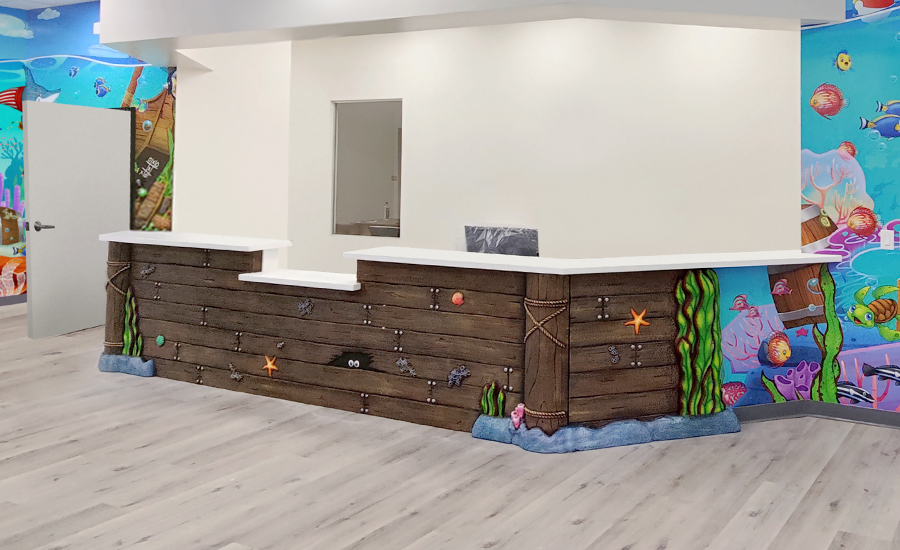 Reception desk with an underwater theme, perfect for a swim facility, featuring cartoon sea creatures and ocean decor. The walls are colorful with fish, corals, and treasure illustrations, creating a playful, aquatic atmosphere.