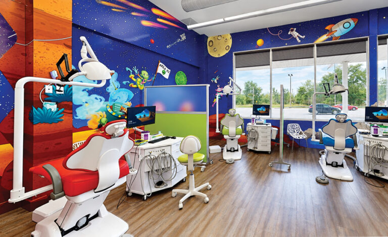 A colorful, space-themed pediatric dental office with three dental chairs, computers, dental equipment, wood flooring, and large windows showing trees and parked cars outside. The walls feature planets, rockets, cartoon characters, and a friendly giant insect soaring among the stars.