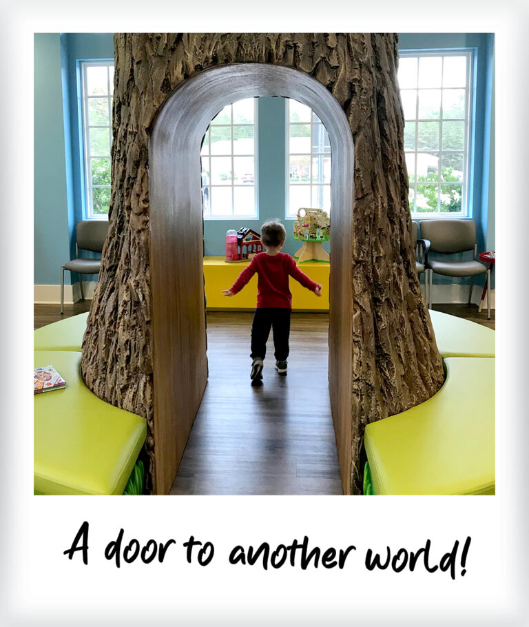 A child in a red shirt walks through a tree-trunk-shaped wall mural archway in a room with light green benches. Text at the bottom reads, A door to another world!.