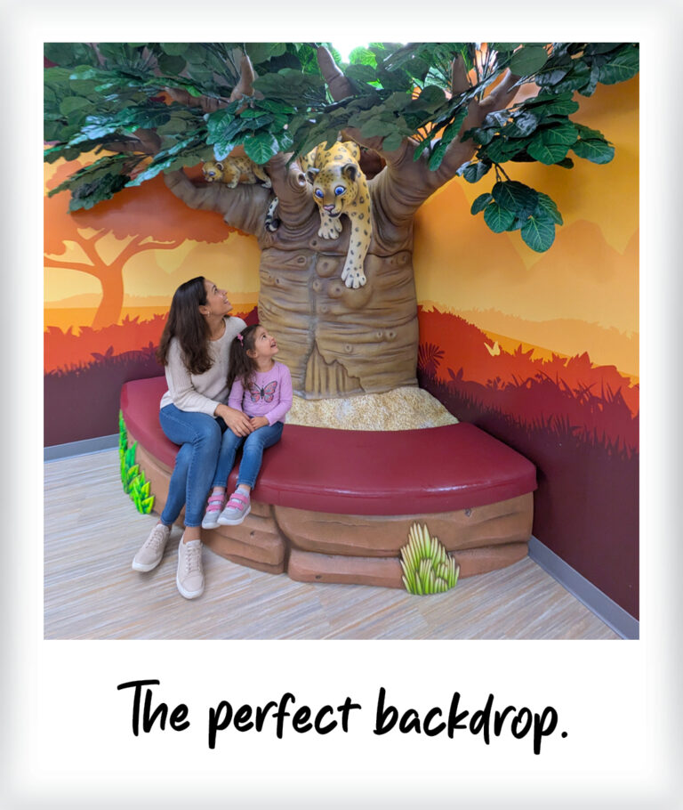 A woman and a young girl sit on a bench in front of a wall mural featuring a leopard sculpture, with the text The perfect backdrop below the image.